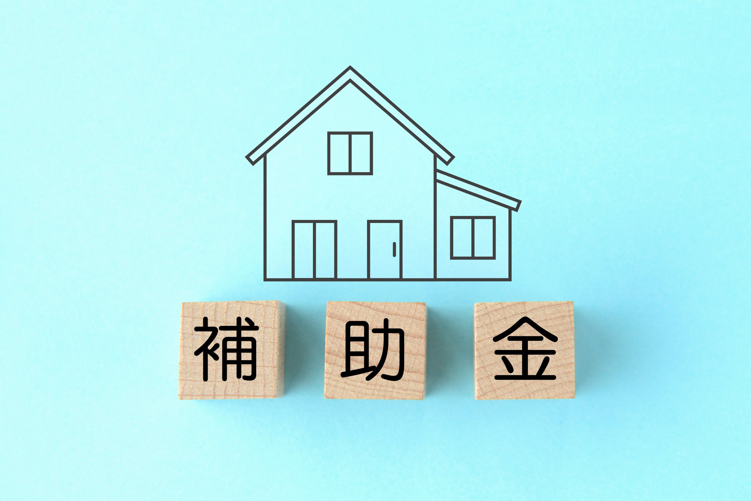 「補助金」と書かれた木製ブロックの上に住宅の線画が描かれた、水色背景のイメージ画像