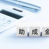 木製ブロックに記された「助成金」の文字と、隣に配置された電卓とペン
