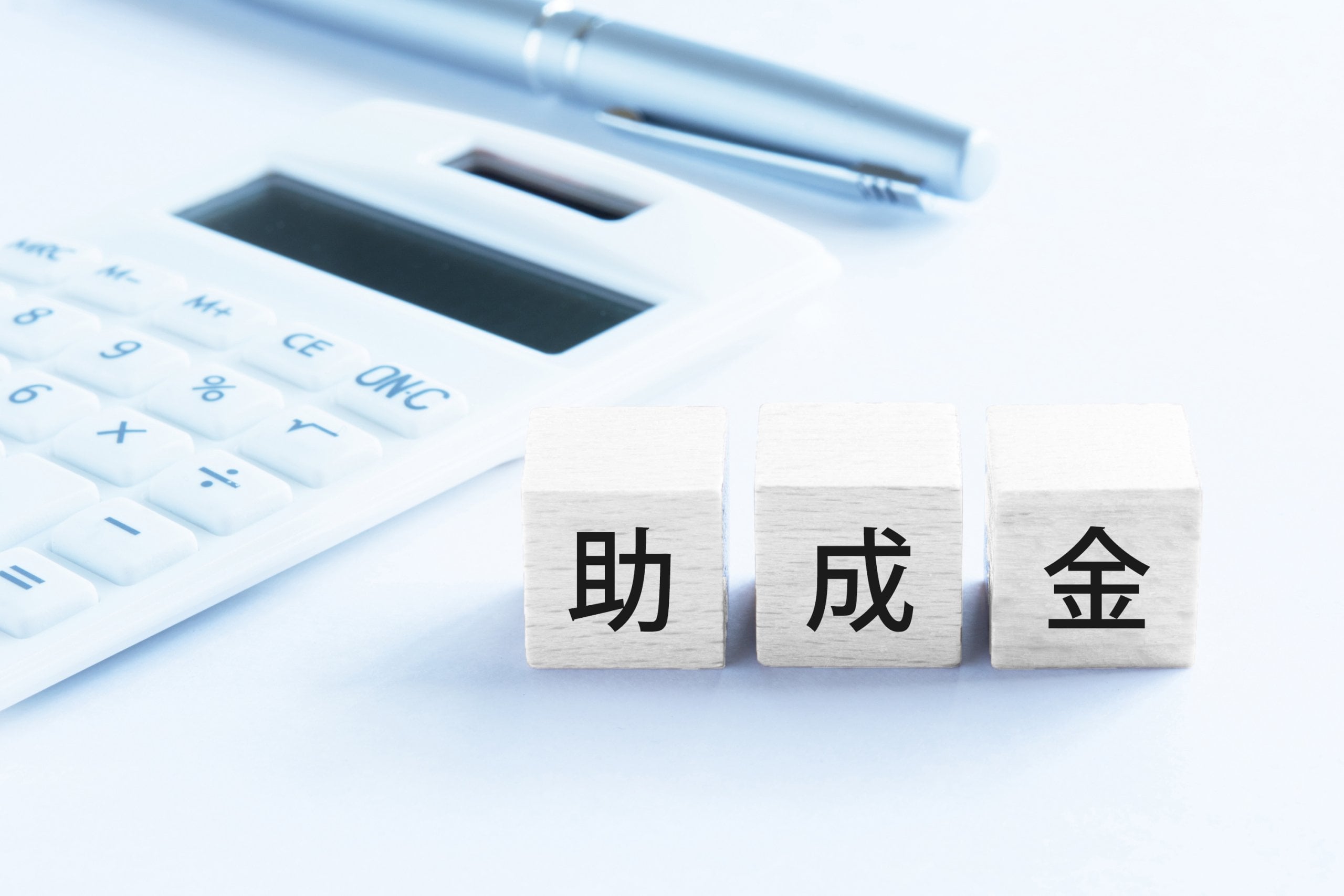 木製ブロックに記された「助成金」の文字と、隣に配置された電卓とペン