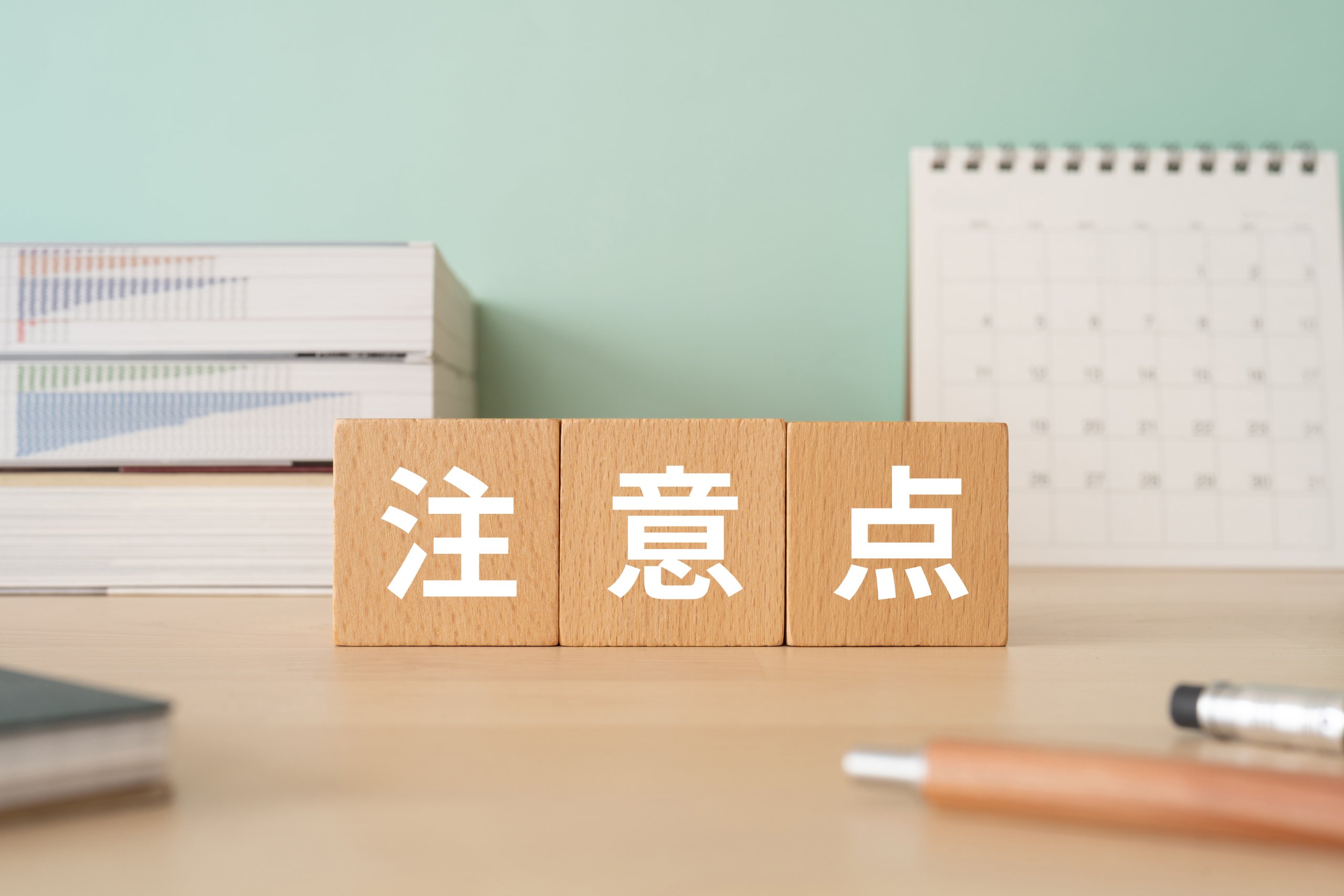 木製ブロックに「注意点」と記され、その周囲に書籍、カレンダー、筆記用具が置かれたデスク